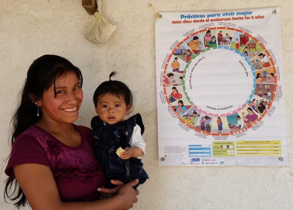 A mother and child stand in front of the Wheel of Practices in Guatemala.